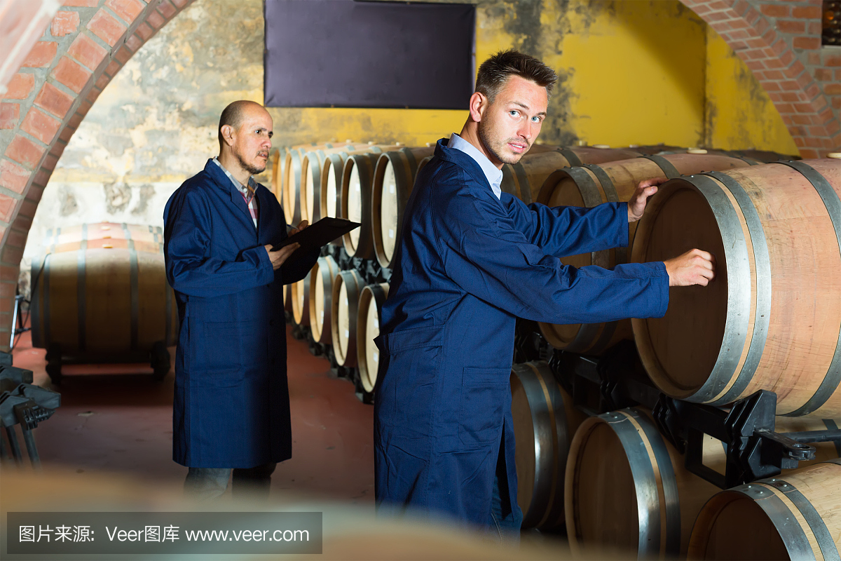 兩個穿著制服的男人微笑著在酒窖里做筆記